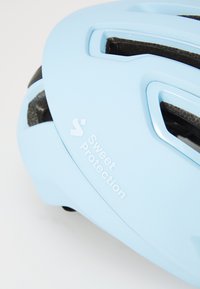 Svetlo modrá cyklistická prilba s ventilačnými otvormi a textúrovaným polstrovaním vo vnútri. Na boku sa nachádza logo "Sweet Protection" v bielej farbe.