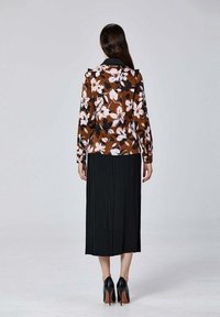 Blouse florale marron avec des fleurs roses, associée à une jupe midi plissée noire. Portée avec des escarpins noirs.