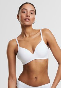 White bra made of smooth fabric. Features a V-neckline, adjustable straps, and a seamless design. No visible closures or embellishments.