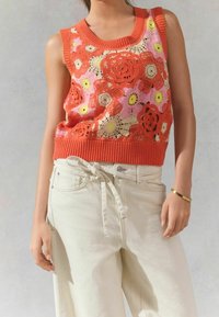 Crochet-kukkamekko oranssina, vaaleanpunaisina ja keltaisina, jossa on ribbireunus kaula-aukossa ja helmassa. Yhdistetty vaaleanbeigeihin, löysän istuvuuden pöriin.