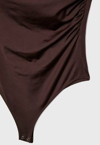 Maillot de bain en tissu brun lisse avec des détails de ruché et un système de fermeture à pression en bas. Présente une silhouette élégante et contournée.