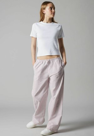 Bílý přiléhavý tričko spárované s lehkými růžovými pruhovanými volnými kalhotami s elastickým pasem a bočními kapsami. Na nohou bílé tenisky.
