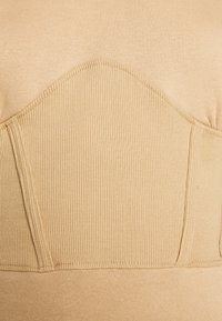 Tejido beige acanalado con un diseño redondeado y paneles texturizados en la parte superior; presenta bordes sin costuras y un acabado suave.