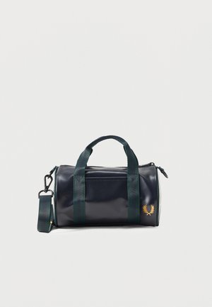 Petit sac cylindrique noir avec des poignées vert foncé et une bandoulière, avec un emblème de couronne de laurier dorée sur le côté.