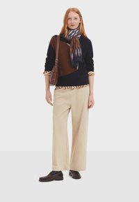 Gestrickter navy- und braunfarbener Pullover mit geometrischem Design, cremefarbene weite Hose, gemusterter Schal und braune Schultertasche. Dunkle Loafer runden das Outfit ab.