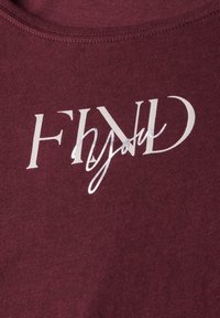 T-shirt bordeaux avec un col rond présentant le texte "FIND you" en lettres blanches et argentées contrastées, mettant en valeur un tissu texturé.