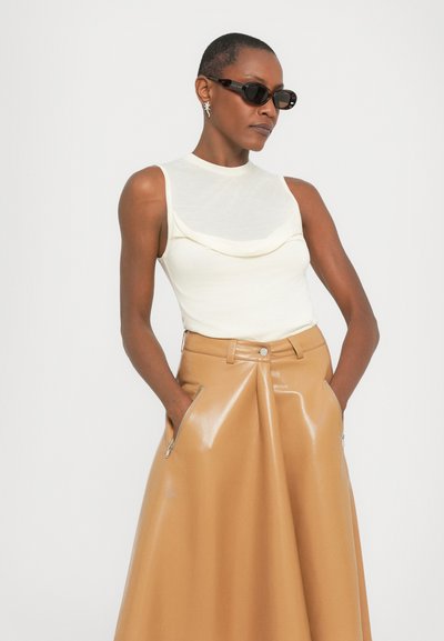 Crème mouwloze top met gedrapeerde details, gecombineerd met een tan hoge taille, glanzende faux leren rok met zijzakken.