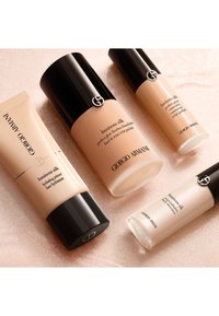 Vier Giorgio Armani Luminous Silk producten: een primer in een beige tube, twee flessen foundation en een highlighter in een glazen tube, allemaal met zwarte doppen.