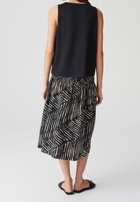 Musta hihaton paita pyöreällä kaula-aukkolla yhdistettynä musta-valkoiseen ajatuksenomaiseen midihameeseen, jossa on geometrisiä viivoja ja elastinen vyötärö.