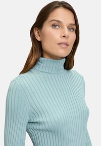 Light blue ribbed turtleneck sweater with a subtle texture, fitted silhouette, and long sleeves, featuring a high neck for added warmth.