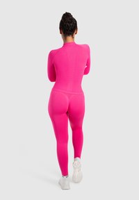 Fitted roze longsleeve bodysuit van textuurstof, met hoge kraag en naadloos design, gecombineerd met witte sportschoenen.