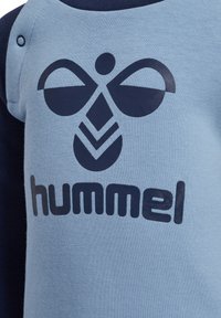 Jasnoniebieska koszula z ciemnoniebieskimi akcentami. Posiada wyraźne ciemne logo oraz napis "hummel". Miękka faktura tkaniny i okrągły dekolt.