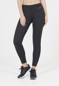 Zwarte sportieve leggings met een hoge tailleband, een zachte textuur en vlakke naden. Gecombineerd met zwarte sneakers voor een sportieve uitstraling.