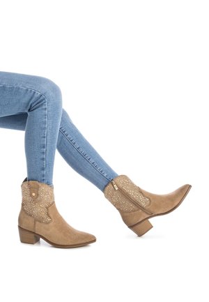 Botas de tobillo de ante color arena con puntas puntiagudas y detalles decorativos en plata. Cuentan con una cremallera lateral y un tacón bajo apilado.