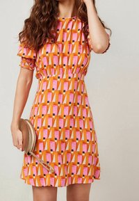 Robe à manches courtes avec un motif géométrique vibrant orange, rose et crème, taille smockée et coupe décontractée. Accessoirisée d'une petite pochette.