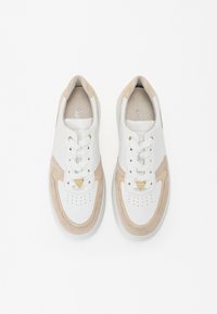 Baskets blanches et beiges en cuir et suède, avec un bout rond, un système de laçage et un détail en forme de cœur.