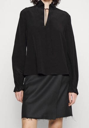 Czarna bluzka z długim rękawem, z kołnierzykiem stójką, dekoltem typu keyhole oraz teksturowanymi koronkowymi akcentami. Połączona z czarną asymetryczną spódnicą z postrzępionym dołem.