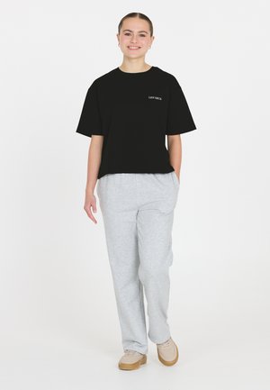 Sort kortærmet t-shirt med hvid tekst, parret med lysegrå, løstsiddende sweatpants og beige sko. En enkel og afslappet påklædning.