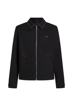 Juoda striukė su užtrauktuku, metalinėmis detalėmis apykaklėje, šoninėmis kišenėmis ir mažu logotipu ant krūtinės. Sukurta su tiesiu apvadu ir ilgomis rankovėmis.