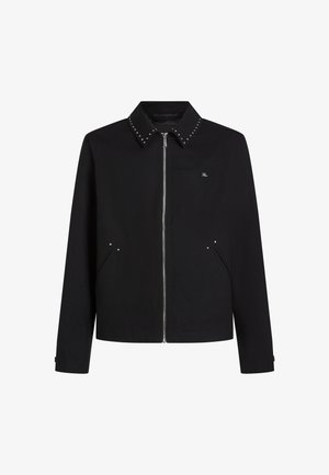 Čierna bunda s potomkovým zapínaním, hrotovaným golierom, bočnými vreckami a malým logom na hrudi. Navrhnutá s rovnými koncami a dlhými rukávmi.