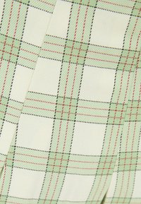 Lätt tyg med ett grönt och rött rutor mönster på en krämfärgad bakgrund. Strukturväv med kontrasterande svart sömnad.