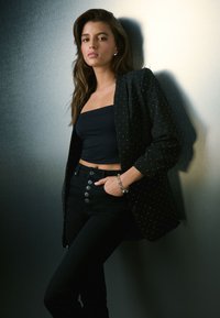 Čierne sako s striebornými cvokmi cez čierny crop top a čierne džínsy s vysokým pásom a gombíkovými detailmi. Strieborný náramok ako doplnok.