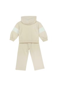 Ensemble beige pour enfant en deux pièces avec sweat à capuche doté de rayures blanches sur les manches et pantalon large assorti, présenté de dos.