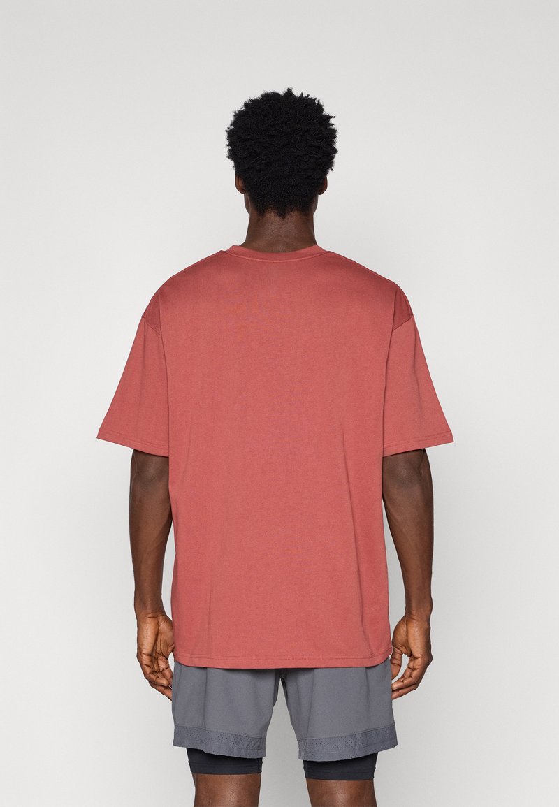 Camiseta de manga corta oversize para hombre en rojo suave, fabricada en un tejido suave con un cuello redondo. La parte de atrás es lisa y tiene un corte relajado.