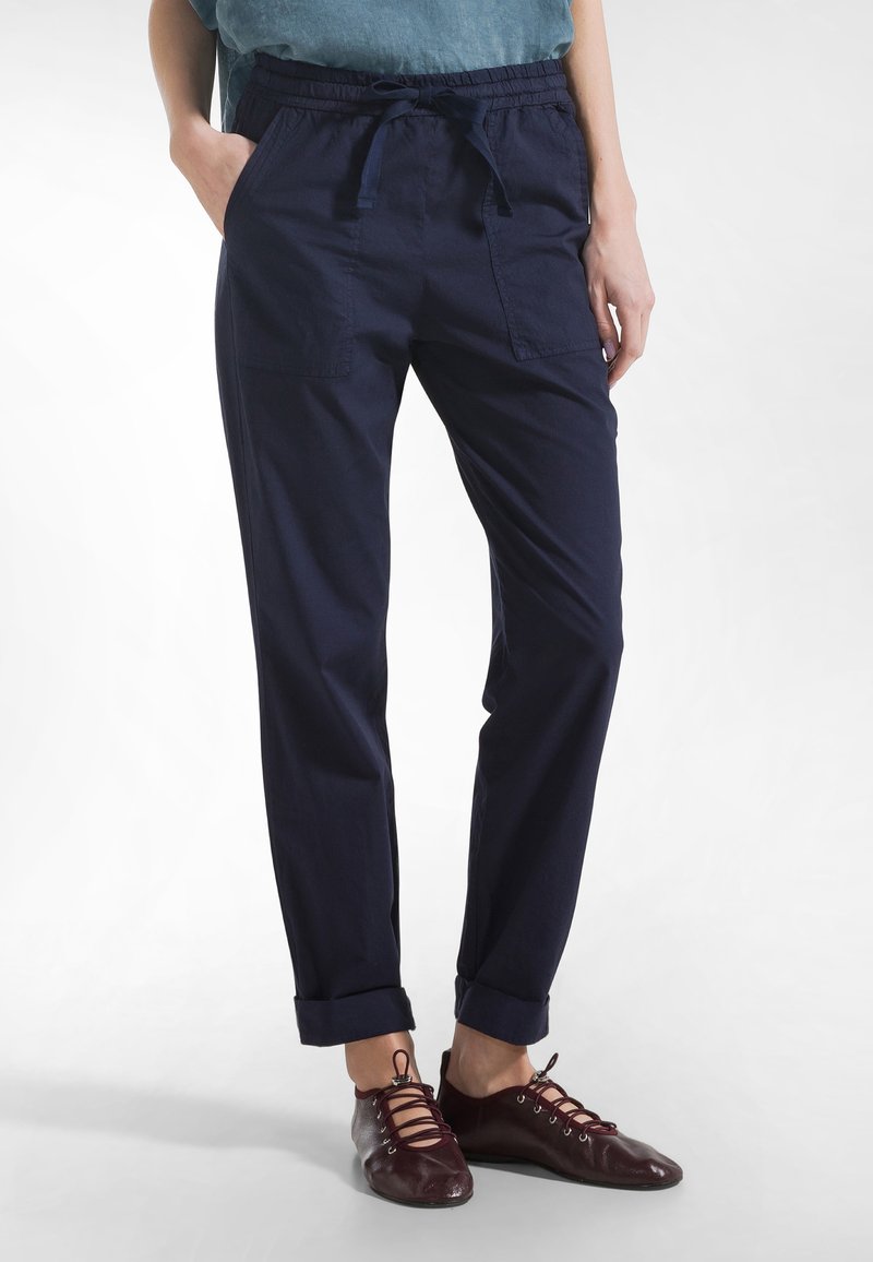 Granatowe, lekkie spodnie wykonane z tkaniny, z elastycznym pasem, sznurkiem do ściągania i podwiniętymi mankietami. Posiadają dwie przednie kieszenie.