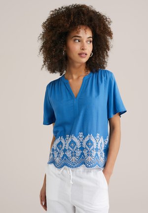 Blue short-sleeve blouse with a V-neckline, featuring white floral embroidery along the hem. Soft fabric with a relaxed fit.