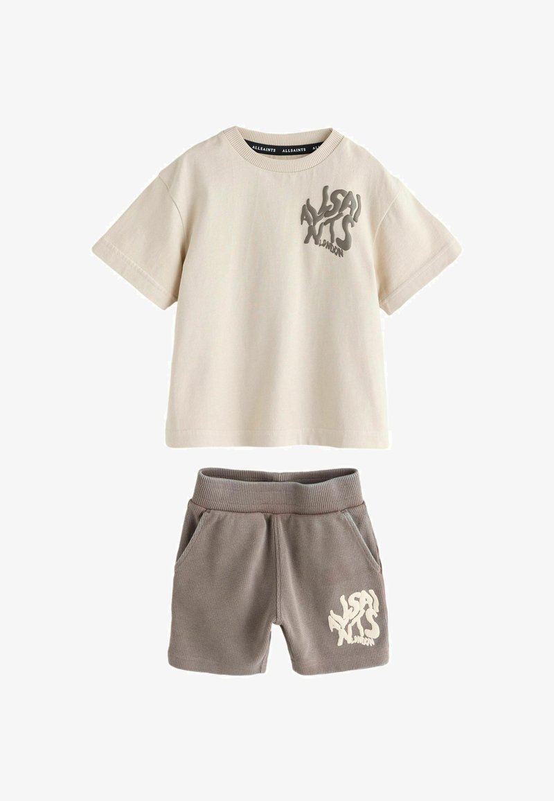 Tricou bej din bumbac cu un logo gri, combinat cu pantaloni scurți texturați gri, cu buzunare laterale și imprimeu cu logo pe picior.