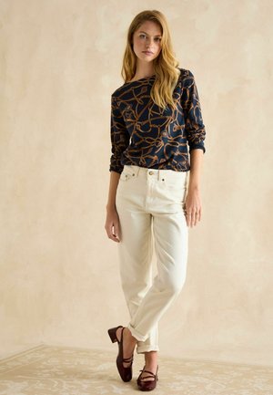 Navy top with a patterned design, cream-colored wide-leg pants, and maroon low-heeled shoes. Smooth fabric and casual fit with rolled sleeves.