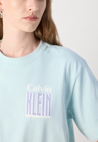 Lichtblauwe katoenen t-shirt met het "Calvin KLEIN" logo in het wit en paars, ontspannen pasvorm, korte mouwen, ronde hals.