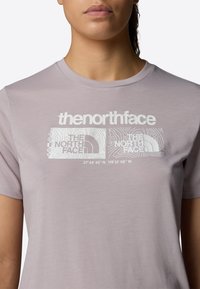 Camiseta de manga corta de color púrpura claro con un estampado gráfico blanco, que incluye texto y un diseño de contorno, con un escote redondo.