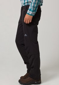 Pantalons outdoor noirs avec une coupe slim, fabriqués à partir de matériau durable. Comprend des poches latérales zippées et un logo Adidas discret sur la cuisse.