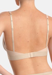 Beige undergarment with adjustable satin straps, smooth fabric, hook-and-eye closure, and logo accents on the band. Back view displayed.