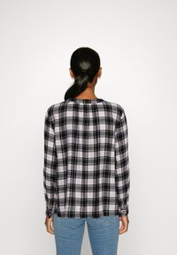 Camicia a quadri bianca e nera con maniche lunghe, polsini abbottonati e vestibilità morbida. Tessuto soffice con orlo dritto e dettaglio della piega centrale sul retro.