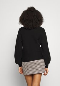 Czarny dzianinowy sweter z balonowymi rękawami, w połączeniu z krótką spódnicą w kratkę houndstooth. Tekstura wydaje się miękka i przytulna.