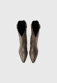 Botas de cuero marrón con punta afilada y costuras decorativas, de textura suave. Cuentan con un tacón bajo y lengüetas para facilitar el calzado.