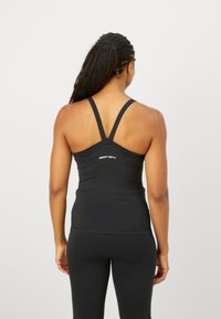 Črn športni top z obliko racerback. Narejen iz elastičnega materiala, ima logotip blagovne znamke na zgornjem delu hrbta. Gladka tekstura.