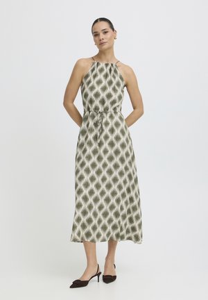 Naine kannab varrukateta oliivirohelise mustriga poolpika kaelusega kleiti, millel on vöötalje pael, ning musti madala kontsaga sling-back kingi.