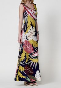 Robe longue avec un fond bleu marine orné de grands motifs de feuilles tropicales multicolores en rouge, jaune et blanc. Tissu lisse et léger.