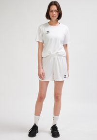 Biały komplet sportowy składający się z koszulki z krótkim rękawem i szortów z elastycznym pasem, oba z czarnym logo. Do kompletu czarne buty i białe skarpetki.