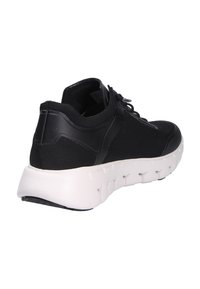 Zapatilla deportiva negra con parte superior de tela de punto, cordones en la parte delantera y suela blanca gruesa con patrones recortados, vista desde un ángulo trasero.