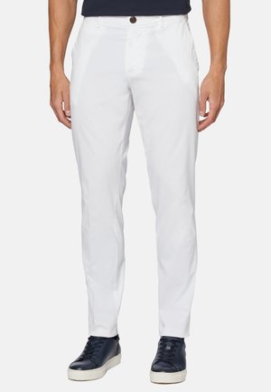 Pantaloni bianchi realizzati in tessuto leggero, con design a gamba dritta, tasche anteriori e chiusura a bottone singolo. Indossati con sneaker scure.