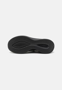 Semelle de chaussure en caoutchouc noir avec un motif de rainures ondulées et des lignes diagonales pour l'adhérence, vue par le dessous sur fond blanc.