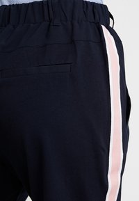 Pantalones azul marino con una textura suave, que cuentan con una cintura elástica y una franja lateral en rosa pálido y blanco. Incluyen un detalle de bolsillo trasero.