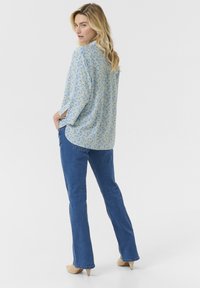 Blusa a maniche lunghe floreale blu con vestibilità rilassata, con scollatura rotonda e spacchi laterali, abbinata a jeans blu a gamba dritta e tacchi beige.