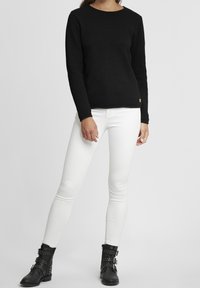 Svart strukturerad långärmad tröja kombinerad med vita smala jeans och svarta ankelskor med spännen och nitar.