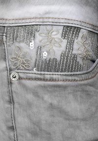Close-up of a light gray denim pocket featuring silver sequins and embroidered floral patterns.
